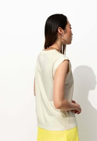Haut sans manches beige clair avec des manches roulées, en tissu doux, et un col rond, associé à une jupe jaune texturée.