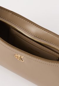 Calvin Klein håndtaske i blød beige læder. Har en guldfarvet lynlås og logo, indvendig kortlomme og glat tekstur med stikninger.