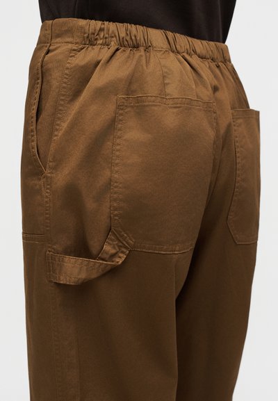 Καφέ παντελόνι cargo με ελαστική μέση, διαθέτει πλαϊνές τσέπες και πίσω τσέπες με πάτο, κατασκευασμένο από ελαφρύ ύφασμα με ομαλή υφή.