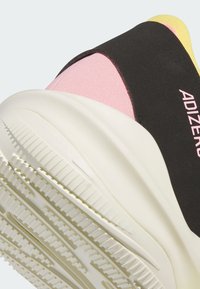 Sort og pink sportsko med en struktureret overdel, hvid mellemsål og en mønstret gummibas. Har "ADIZERO" branding på siden.