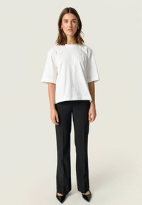White short-sleeve cotton t-shirt with a pocket, paired with black tailored trousers and pointed black heels. Simple, clean design.