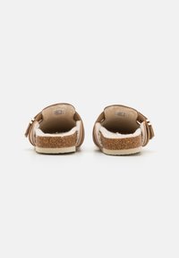 Brune slip-on sko med en teksturert korksåle og myk innvendig foring. Har justerbare stropper og et avrundet bakdesign.