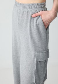 Graue Jogginghosen aus weichem Material, mit elastischem Bund und Seitentaschen, sowie einer Cargotasche am Oberschenkel.