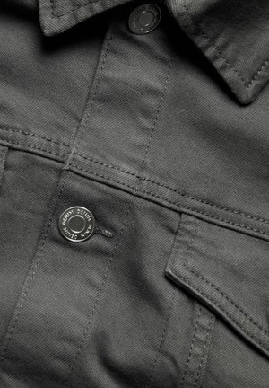 Grijze denimstof met een gestructureerde afwerking, voorzien van een knoopsluiting en een borstzak. Stikdetails zijn zichtbaar langs de naden.