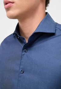 Men's blue button-up shirt with a collared neckline. Fabric has a smooth texture, featuring dark buttons and a tailored fit.