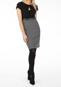Haut noir avec un détail en forme de trou de serrure et des manches courtes, associé à une jupe crayon grise ajustée et des collants noirs, terminé par des talons noirs.