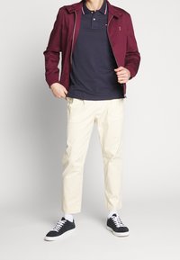 Bordeaux bluza z zamkiem, granatowa koszulka polo, beżowe spodnie i czarne trampki. Cechy to kołnierz, kontrastowe paski oraz białe skarpetki.