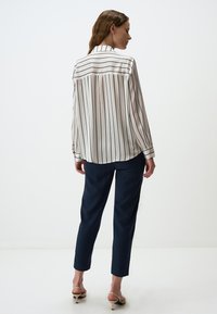 Weiße Bluse mit blauen Streifen, lockere Passform, lange Ärmel und klassischer Kragen, kombiniert mit blauen schmal geschnittenen Hosen und Absatzsandalen.