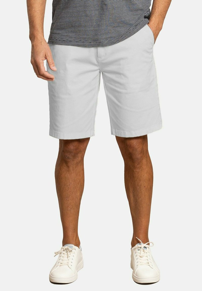 Shorts de algodón blancos con corte recto, bolsillos laterales y una textura suave, combinados con zapatillas blancas y una camisa estampada.