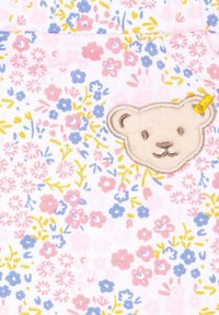 Blumengemusteter Stoff in Rosa, Blau und Gelb mit einem weichen gestickten Bärenpatch, der ein hellbraunes Gesicht zeigt.