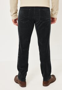 Schwarze Cordhosen mit strukturierter Oberfläche, ausgestattet mit Gesäßtaschen und einem geraden Bein. Kombiniert mit braunen Schuhen und einem Stricktop.