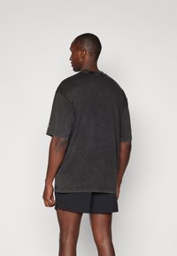 Schwarzes, übergroßes Baumwoll-T-Shirt mit Rundhalsausschnitt, kurzen Ärmeln und sichtbaren Steppnähten, getragen mit dunklen Shorts.