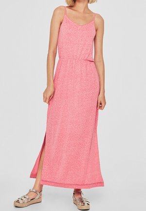 Vrouw in een mouwloze roze maxi-jurk met een zijsplit en zilveren sleehakken tegen een effen achtergrond.