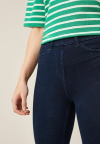 Zielono-biały, w paski, krótki top połączony z ciemnoniebieskimi, dopasowanymi dżinsami. Materiał wydaje się miękki, o gładkiej teksturze i denimu.