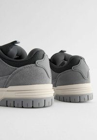 Grå sneakers lavet af en kombination af ruskind og mesh-materialer, med en struktureret sål, fremtrædende syninger og en formet detalje på hælen.