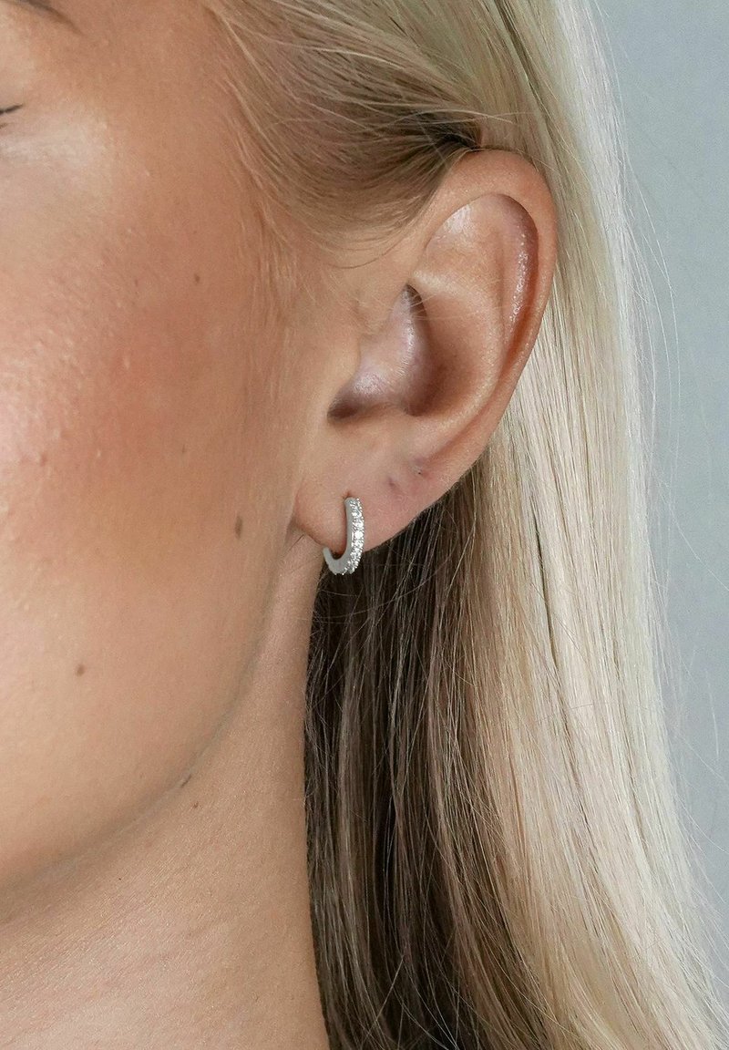 Söljhänge i silver med en texturerad yta, med en rad av små klara kristaller längs den framträdande kanten. Närbild på örat.