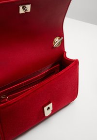 Interno di borsa in velluto rosso con tasca con zip e slot per card. Presenta una chiusura e dettagli in oro. Texture morbida, design strutturato.