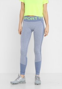 Legginsy sportowe o wysokim stanie w jasnoniebieskim kolorze z teksturowanym wzorem i kontrastującymi ciemnoniebieskimi akcentami. Posiadają zielony pas w stylu "SPORT".