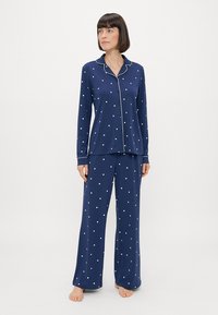 Ναυτικό πιτζάμα σετ με μακριά μανίκια και παντελόνι, διαθέτει λευκό μοτίβο καρδιές και αντίθεση στα περιγράμματα του γιακά και των μανικιών. Μαλακό ύφασμα.