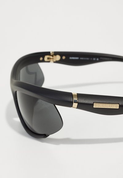 Ochelari de soare negri cu un finisaj mat, având lentile închise la culoare. Accente aurii pe bratul ochelarilor și detalii de brand pe lateral. Design elegant.