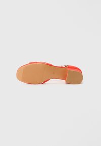 Offene High Heels aus Veloursleder in lebhaftem Orange mit einer hellbraunen Gummisohle, die über strukturierte Abschnitte für besseren Halt verfügt.