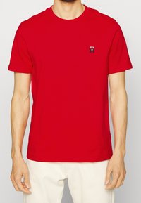 T-shirt in cotone rosso con maniche corte, colletto rotondo e un piccolo logo ricamato sul lato sinistro del petto. Tessuto liscio, vestibilità regolare.