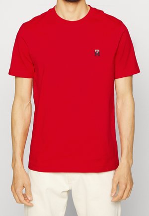 T-shirt en coton rouge à manches courtes, col rond, avec un petit logo brodé sur la poitrine gauche. Texture lisse, coupe classique.