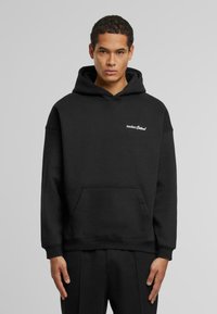 Sudadera de algodón negra con un bolsillo frontal y puños acanalados, que presenta el logotipo en texto blanco "Another Cotton" en la parte superior del pecho izquierdo.