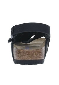 Sandalia de ante negra con suela de corcho, correa ajustable y planta texturizada. Presenta un tacón plano y un diseño minimalista de apertura trasera.