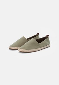 Gröna canvas slip-on skor med rund tå, med en vävd jutesula och små bruna hälaccenter.