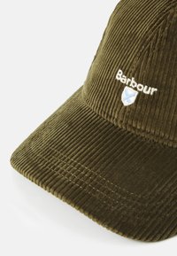 Casquette en velours côtelé vert olive avec logo Barbour brodé et blason à l'avant, dotée d'une visière incurvée sur fond blanc.