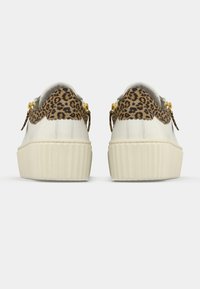 Valkoiset nahkakengät, joissa leopardikuvioiset yksityiskohdat ja kullanväriset metalliosat. Pohja on paksu, uurrettu ja taustassa on teksturoidut yksityiskohdat.