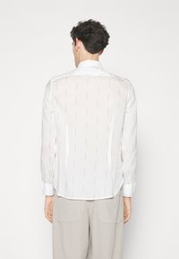 Biała, koszula z długim rękawem o przezroczystej fakturze i subtelnym wzorze. Posiada klasyczny kołnierzyk i zapinane mankiety.