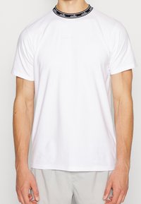 Vit t-shirt med kort ärm och svart ribbad krage som har en logotyp. Tillverkad av bomull, den har en avslappnad passform och slät textur.