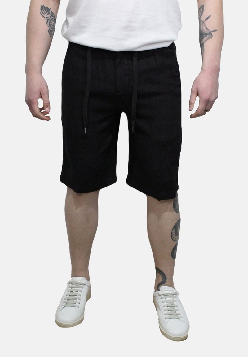 Pantaloni corti neri realizzati in tessuto leggero, dotati di una vita elastica con cordini e tasche laterali. Abbinati a Sneakers bianche.