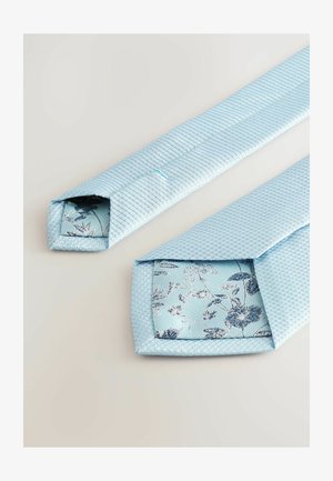 Svetlomodrá textúrovaná kravata s tkaným vzorom, ktorá má na konci kvetinovú saténovú podšívku v odtieňoch modrej a striebornej.