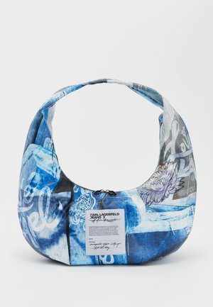 Sac hobo en tissu bleu présentant différentes textures et motifs, avec une fermeture éclair et une étiquette contenant des instructions d'entretien et des détails de marque.