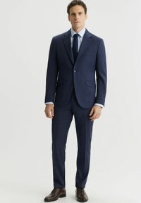 Granatowy garnitur w kratkę o dopasowanym kroju, jednorzędowa marynarka, klapy z ząbkami, dopasowane spodnie oraz brązowe skórzane buty eleganckie.