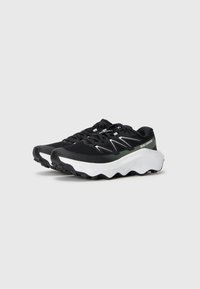 Chaussures de sport noires en maille et caoutchouc, avec une semelle blanche épaisse et texturée, un design en zigzag distinct et des accents gris contrastants.