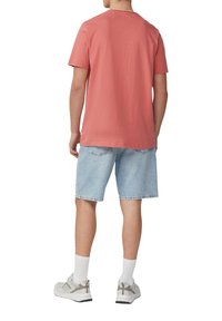 Licht koraalkleurig shirt met korte mouwen, ontspannen pasvorm, gecombineerd met knielange lichtblauwe denim shorts. Witte crew-sokken en grijze sportschoenen.