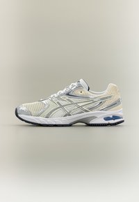 Scarpa da corsa leggera in mesh crema e grigio, con dettagli riflettenti, suola ammortizzata e suola esterna in gomma resistente.