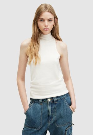 Top bianco senza maniche in un morbido tessuto a costine, caratterizzato da una vestibilità rilassata e da un colletto alto, abbinato a pantaloni in denim blu.