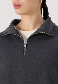 Temno siva zip-jacket s ovratnikom, izdelana iz mehkega materiala. Ima srebrno zadrgo in strukturiran notranji ovratnik.