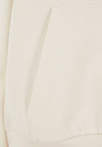 Lys beige sweatshirtstoff med en frontlomme, ribbet tekstur og elastisk hem med subtile sømdetaljer.