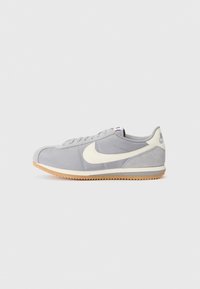 Gray suede sneakers with white accents, featuring a rounded toe, lace-up design, and textured gum sole; minimal branding on heel.