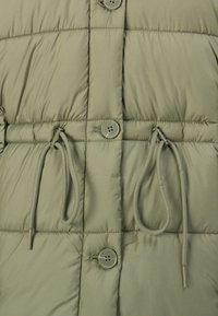 Chaqueta de plumas en un verde oliva apagado, con un diseño acolchado, cordones y cierres de botón. Textura suave con un ligero brillo.