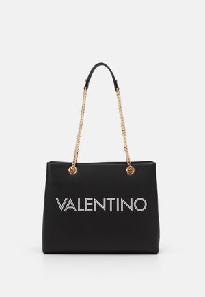 Czarna torba typu tote Valentino z białym logo, złotymi łańcuszkowymi rączkami i czarnym skórzanym uchwytem na białym tle.