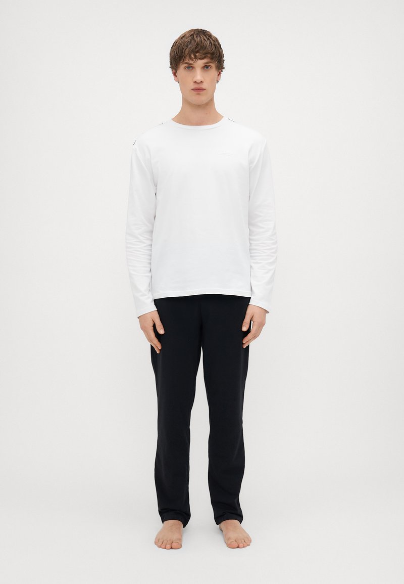 Pikao valge pikkade varrukatega T-särk, millel on ümar kaelus, koos mustade pükstega. Särgile on iseloomulik minimaalne detaliseeritus ja sile tekstuur.