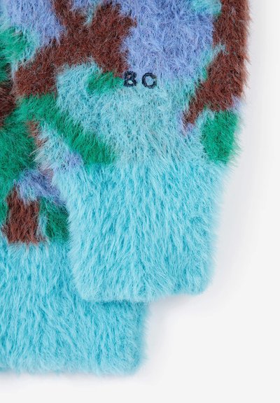 Gros plan d'une manche de pull en maille duveteuse avec un motif camouflage bleu, vert, marron et violet et les lettres "BC" brodées en noir.
