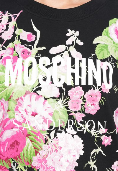 Melna auduma ar dzīvotspējīgiem ziedu motīviem rozā un zaļā krāsā, ar izciliem baltiem uzrakstiem "MOSCHINO" un "SANDERSON of LONDON."